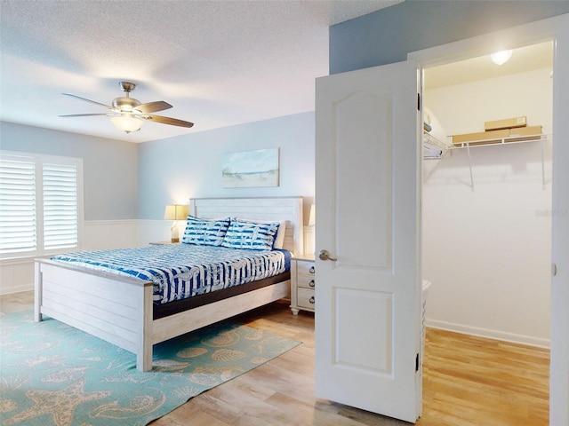 bedroom with a wainscoted wall, a spacious closet, a ceiling fan, a textured ceiling, and wood finished floors