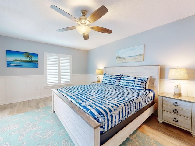 bedroom featuring a wainscoted wall, ceiling fan, and light wood finished floors