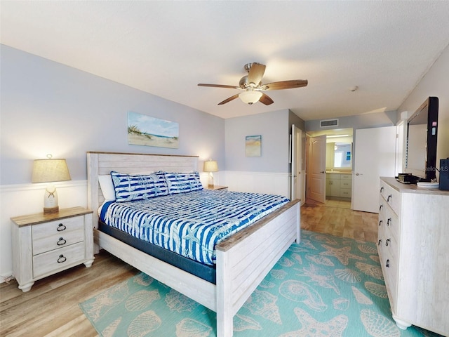 bedroom featuring light wood finished floors, ceiling fan, visible vents, and connected bathroom