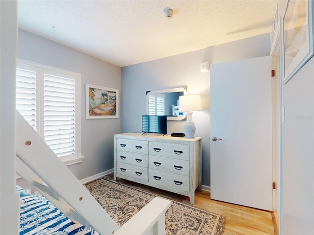 bedroom featuring light wood-style floors, baseboards, and a textured ceiling