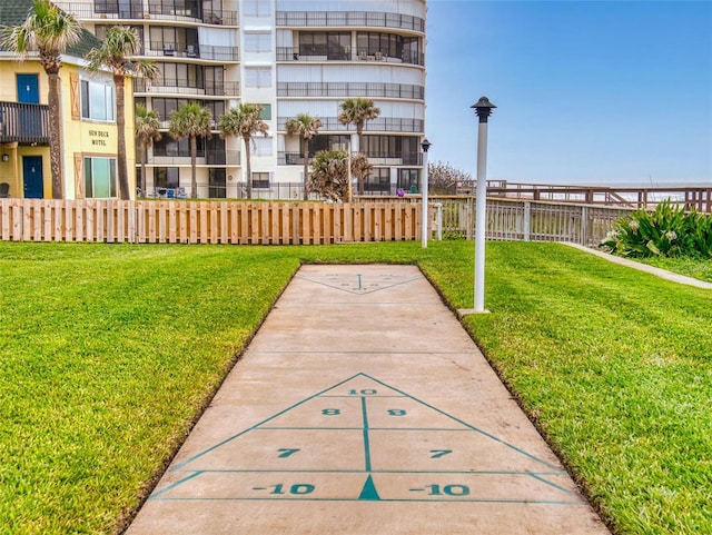 view of home's community featuring shuffleboard, a lawn, and fence