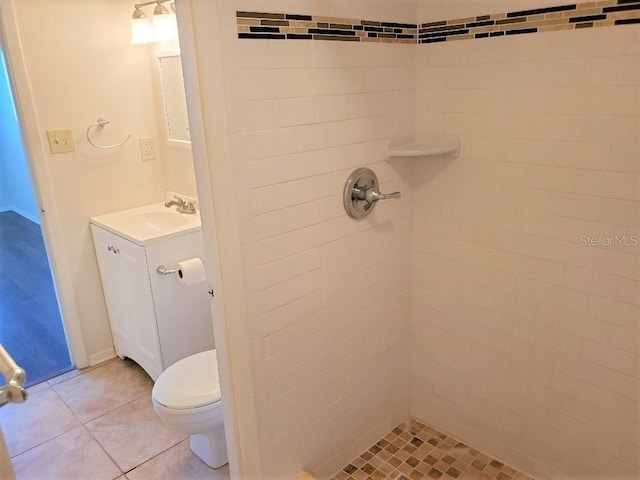 bathroom with tile patterned flooring, tiled shower, vanity, and toilet