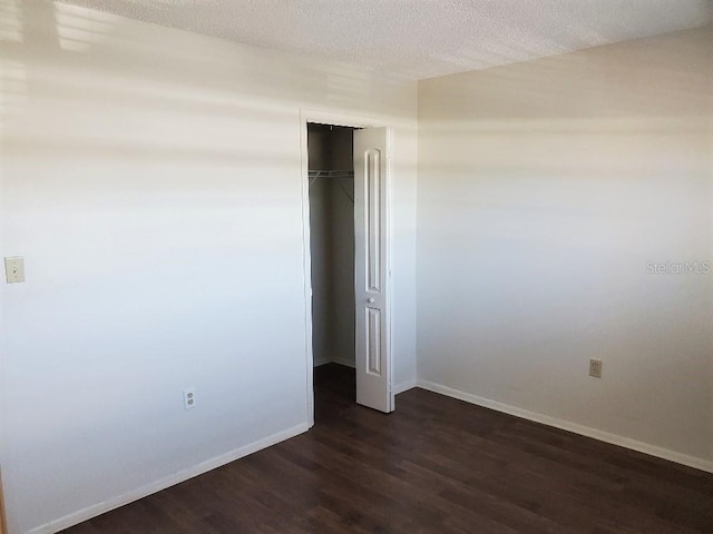 unfurnished bedroom featuring dark wood-style floors, a textured ceiling, baseboards, and a closet