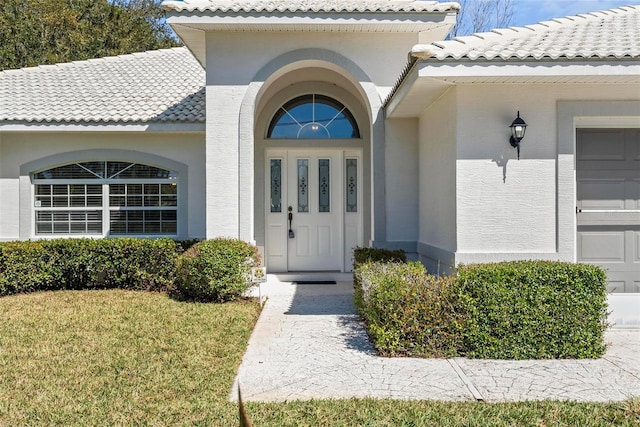 property entrance with an attached garage, a tile roof, a lawn, and stucco siding