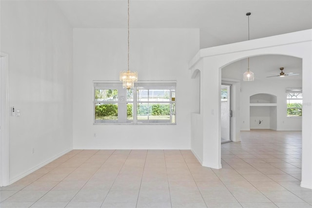 spare room with arched walkways, a towering ceiling, light tile patterned flooring, baseboards, and ceiling fan with notable chandelier