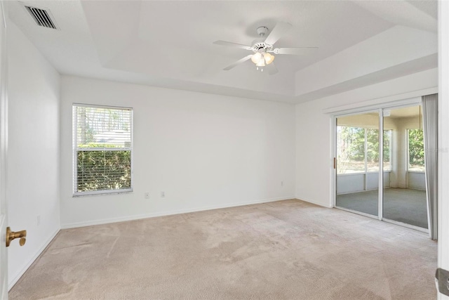 unfurnished room with light colored carpet, a tray ceiling, visible vents, and plenty of natural light