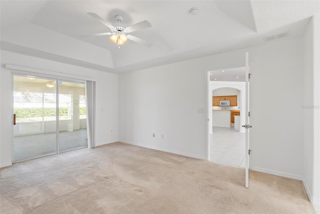 unfurnished room with a tray ceiling, light colored carpet, ceiling fan, and visible vents