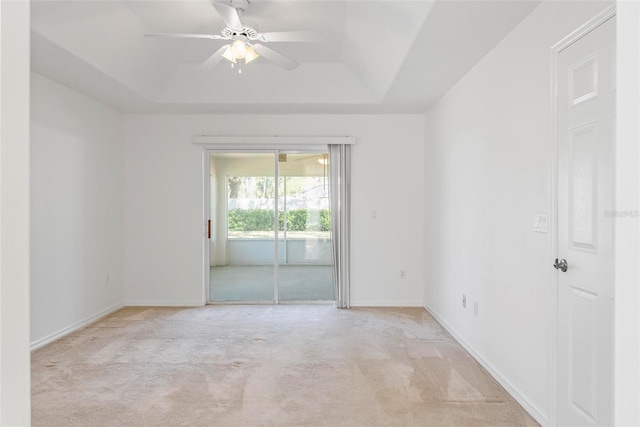 empty room featuring light carpet, ceiling fan, baseboards, and a raised ceiling