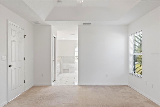 unfurnished room with light carpet, baseboards, visible vents, and a tray ceiling