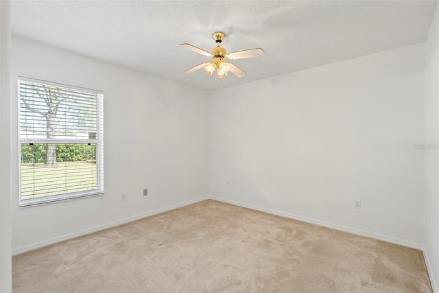 empty room featuring a ceiling fan, light colored carpet, and baseboards