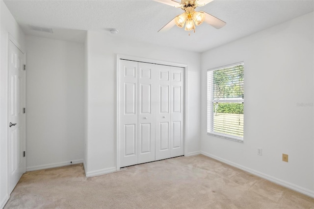 unfurnished bedroom with light carpet, a textured ceiling, baseboards, and a closet