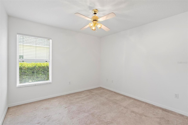 spare room featuring light carpet, ceiling fan, and baseboards