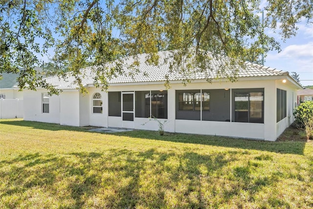 rear view of property with a sunroom, a lawn, a tiled roof, and stucco siding