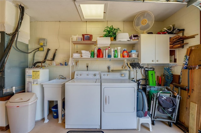 washroom featuring washer and dryer, cabinet space, concrete block wall, and water heater