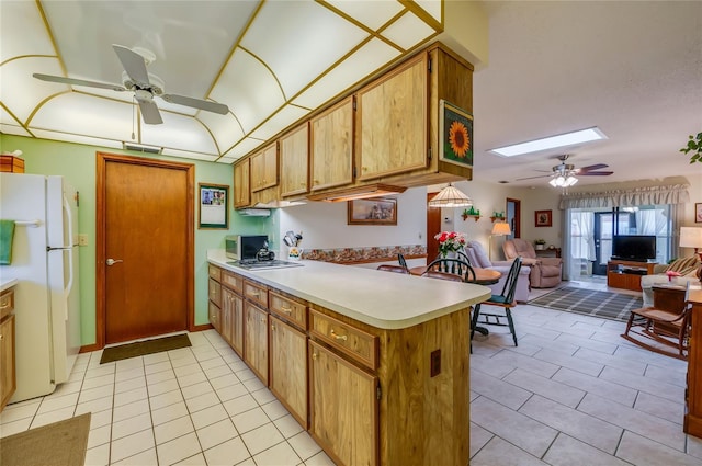 kitchen featuring a skylight, light tile patterned floors, freestanding refrigerator, a peninsula, and light countertops