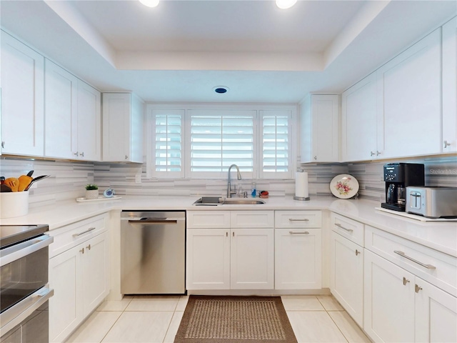 kitchen with appliances with stainless steel finishes, a raised ceiling, a sink, and light tile patterned floors