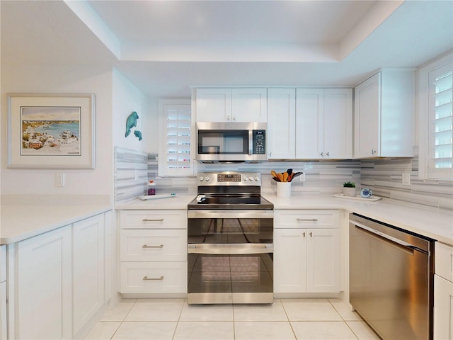 kitchen with stainless steel appliances, tasteful backsplash, a raised ceiling, and white cabinets