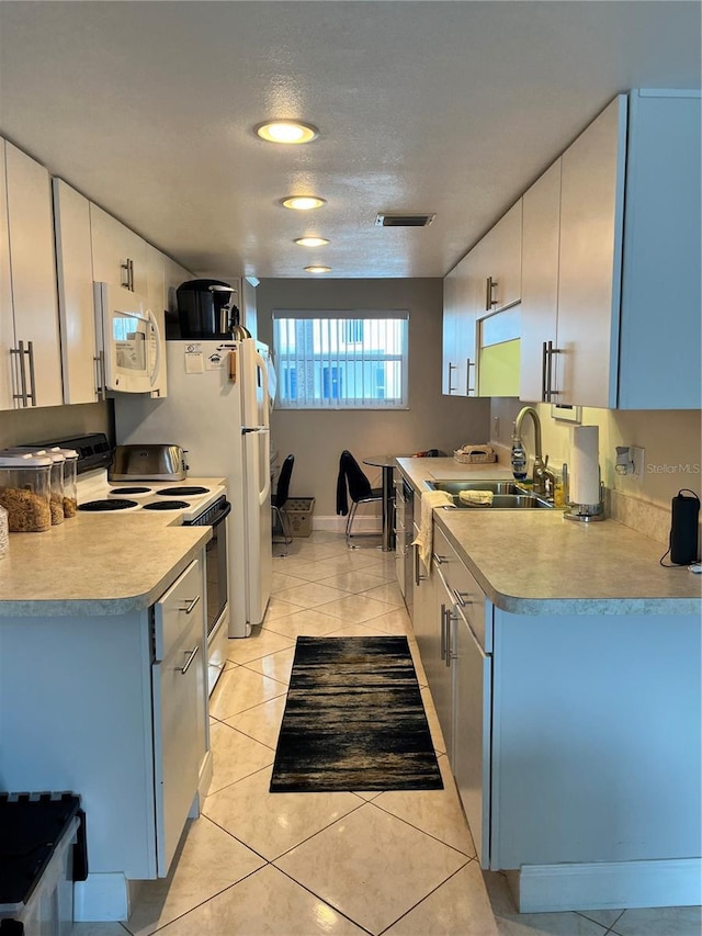 kitchen with light tile patterned floors, electric range oven, white microwave, light countertops, and a sink