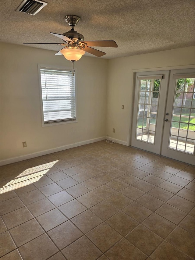 tiled empty room with baseboards, visible vents, a ceiling fan, a textured ceiling, and french doors