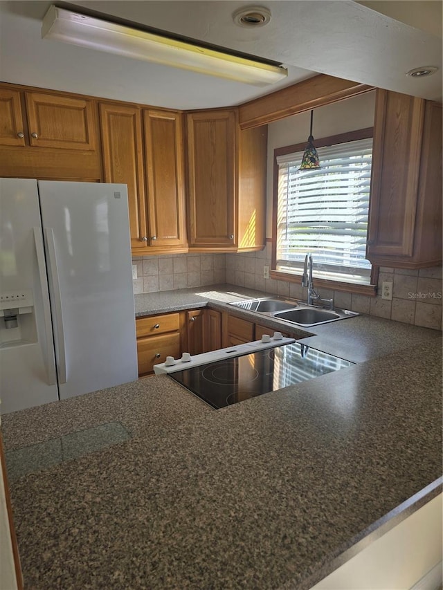 kitchen with tasteful backsplash, white fridge with ice dispenser, brown cabinetry, and a sink