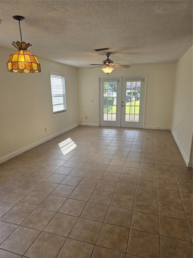 empty room featuring a textured ceiling, tile patterned flooring, visible vents, and baseboards