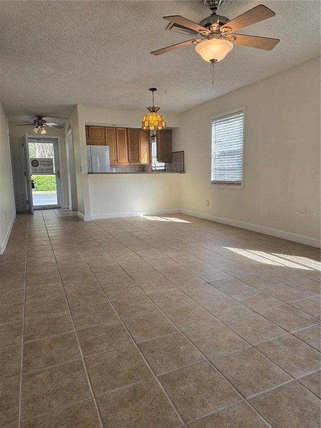 unfurnished living room featuring tile patterned flooring, ceiling fan, a textured ceiling, and baseboards