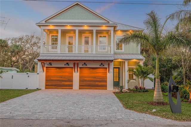 coastal home featuring decorative driveway, a gate, a balcony, and a standing seam roof