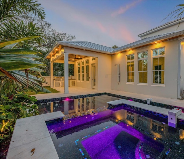 pool at dusk featuring a patio, an outdoor kitchen, a jacuzzi, and an outdoor pool