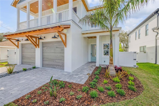 exterior space featuring decorative driveway, stucco siding, a gate, fence, and a balcony