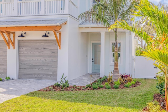 property entrance featuring stucco siding, a lawn, a balcony, a garage, and driveway