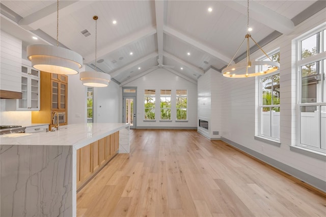 kitchen featuring pendant lighting, vaulted ceiling with beams, light wood-style flooring, glass insert cabinets, and open floor plan