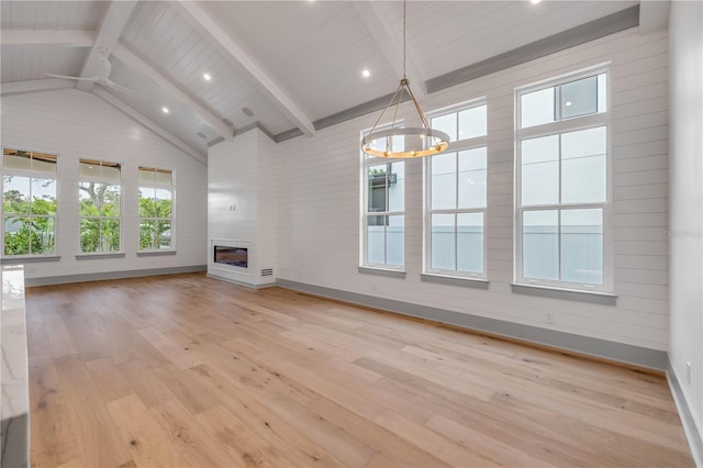 unfurnished living room featuring lofted ceiling with beams, light wood-style floors, a chandelier, and a glass covered fireplace