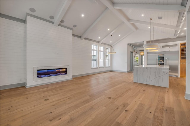 unfurnished living room featuring light wood-style flooring, a glass covered fireplace, high vaulted ceiling, beamed ceiling, and baseboards