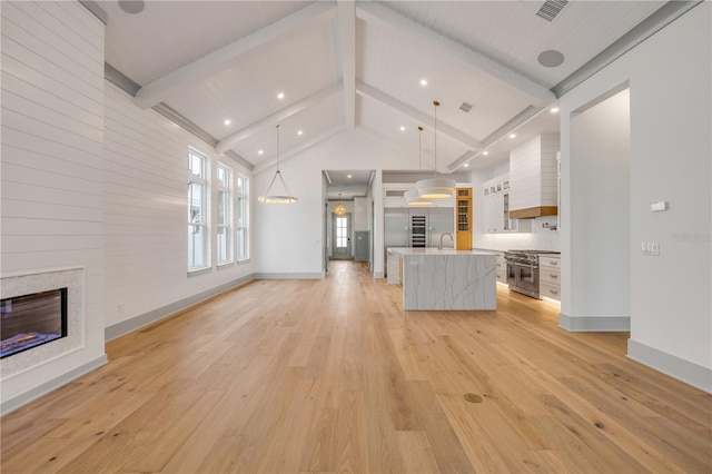 unfurnished living room featuring visible vents, a glass covered fireplace, a sink, light wood-type flooring, and beam ceiling