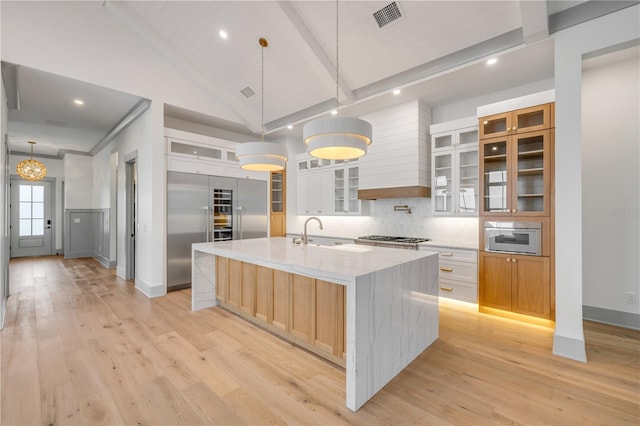 kitchen with beamed ceiling, a spacious island, a sink, and light wood-style flooring