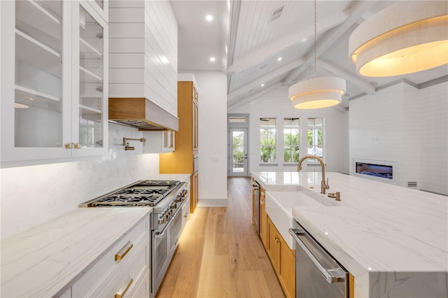 kitchen featuring glass insert cabinets, light wood-style flooring, stainless steel appliances, a sink, and a large island with sink