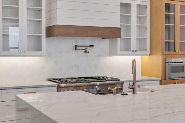 kitchen with light stone counters, oven, premium range hood, and white cabinetry