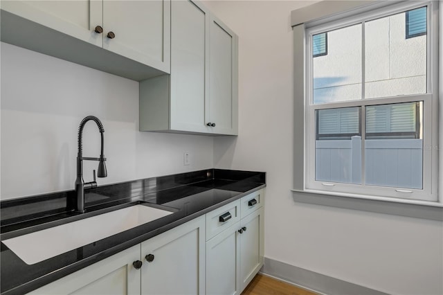 kitchen featuring baseboards, white cabinets, dark countertops, wood finished floors, and a sink