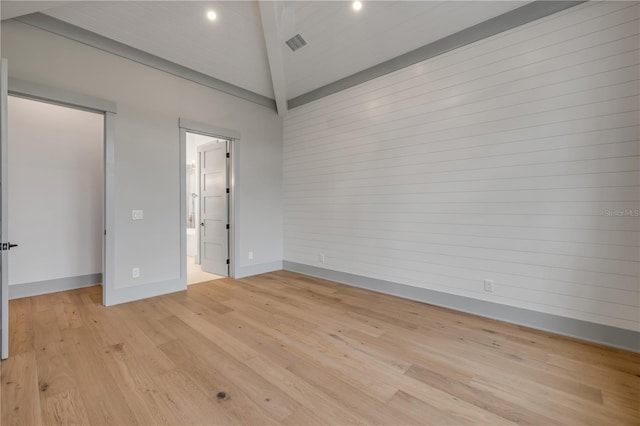 empty room featuring lofted ceiling, light wood finished floors, visible vents, and baseboards