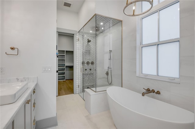 full bath featuring visible vents, tiled shower, vanity, a freestanding tub, and tile walls