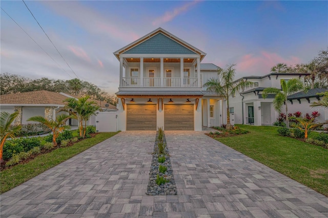 beach home with decorative driveway, a gate, a balcony, a garage, and a front lawn