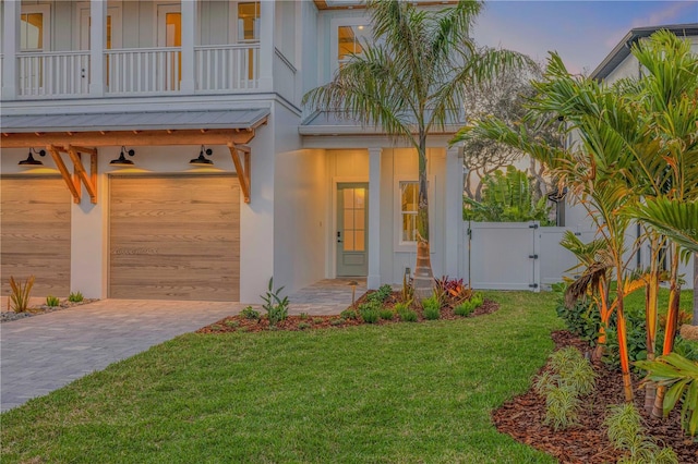 view of front facade with a balcony, a garage, a yard, decorative driveway, and a gate