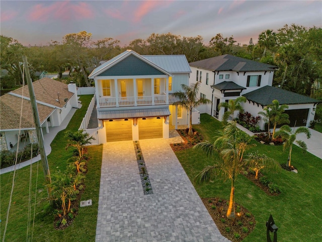 coastal home featuring a balcony, a garage, fence, decorative driveway, and a lawn