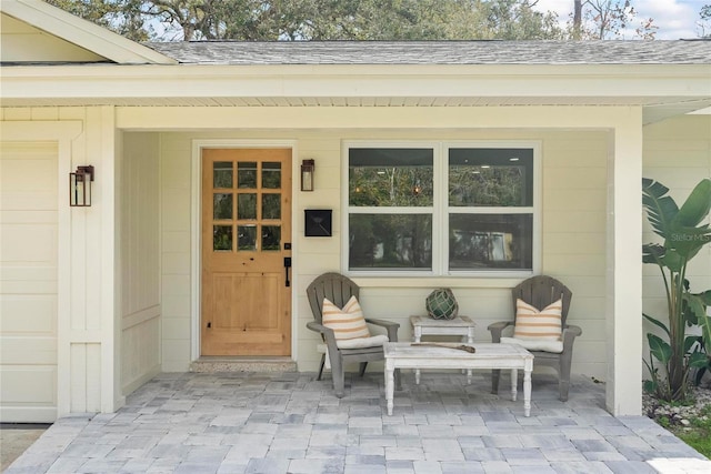 view of exterior entry featuring a shingled roof and a patio area