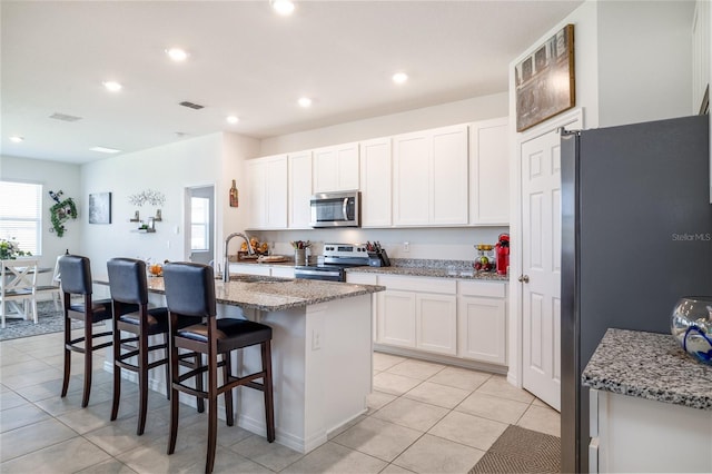 kitchen featuring visible vents, appliances with stainless steel finishes, light stone countertops, white cabinetry, and a sink