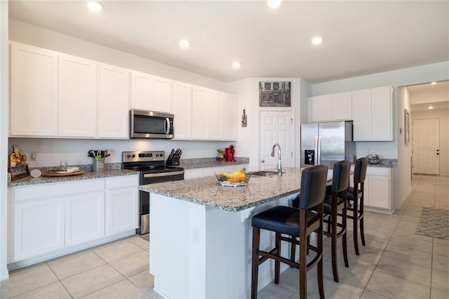 kitchen featuring an island with sink, appliances with stainless steel finishes, a breakfast bar, light stone countertops, and a sink