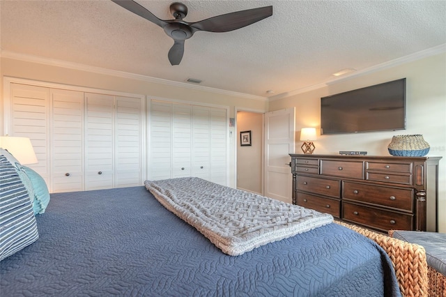 bedroom featuring visible vents, ornamental molding, a textured ceiling, carpet floors, and two closets