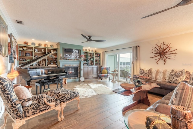 living area featuring visible vents, a tile fireplace, wood finished floors, crown molding, and a textured ceiling