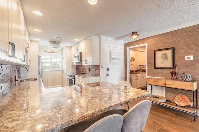 kitchen featuring a breakfast bar, wood finished floors, a sink, appliances with stainless steel finishes, and light stone countertops