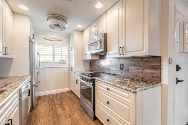 kitchen with backsplash, appliances with stainless steel finishes, a textured ceiling, light stone countertops, and light wood-type flooring